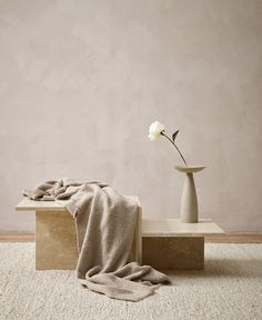 a white flower sitting on top of a wooden bench next to a vase filled with flowers