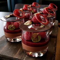 four desserts are arranged on a wooden tray with chocolate and raspberry toppings