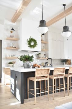 a kitchen with white cabinets and black island in the center is decorated with greenery