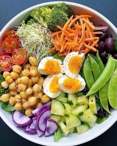 a white bowl filled with lots of vegetables and hard boiled eggs on top of it