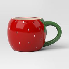 a red and green coffee cup with white dots on it's rim, sitting in front of a gray background