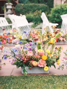 an arrangement of colorful flowers on the ground in front of white chairs and lawn furniture