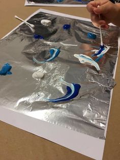 someone is painting something blue and white on a piece of tin foil with toothbrushes