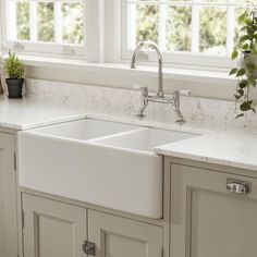 a white kitchen sink sitting under a window next to a potted plant on top of a counter