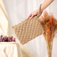 a woman holding a crocheted purse in her hand next to a vase with grapes