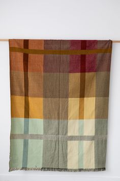 a multicolored blanket hanging on a wall with a wooden hanger in front of it