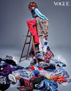 a woman sitting on top of a chair surrounded by clothes