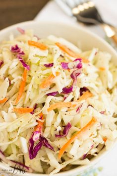 a white bowl filled with coleslaw on top of a table next to silverware