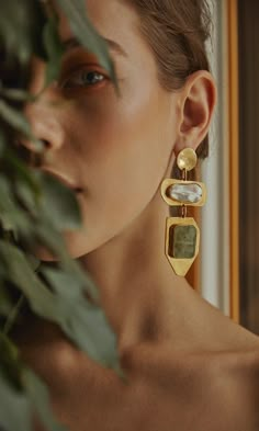 a woman wearing gold earrings and looking at the camera with an instagramr on her phone