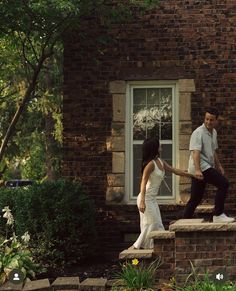 a man and woman holding hands on the steps of a brick building in front of a window