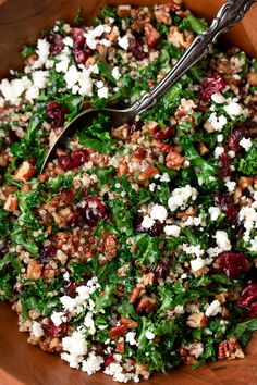 a wooden bowl filled with greens and cranberries next to a metal utensil