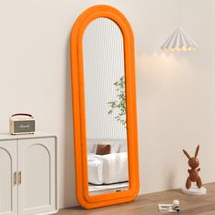 an orange mirror sitting on top of a table next to a white cabinet and lamp