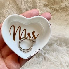 a white heart shaped dish with a wedding ring in the shape of a mr and mrs