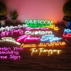 neon signs are lit up on the floor in front of potted plants and trees