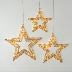 three star shaped lights hanging from strings on a white wall, one is gold and the other is silver