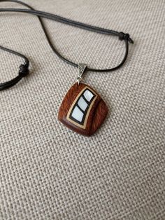 a wooden necklace with white and black designs hanging from a cord on a beige surface