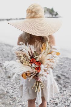 a woman wearing a straw hat and holding a bouquet of flowers in her hands on the beach