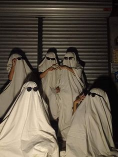 several people dressed in white covering their faces and hands with ghost like costumes around them