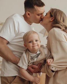 a man and woman kissing a baby boy on the cheek while standing next to each other