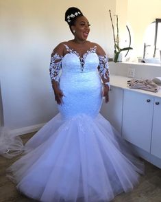 a woman in a white wedding dress standing next to a mirror and looking at the camera