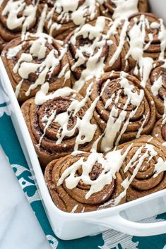 a pan filled with cinnamon rolls covered in white icing and drizzled