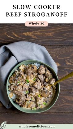 a bowl filled with beef and potatoes on top of a wooden table next to a napkin