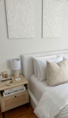 a bedroom with two paintings on the wall and a white bed in front of it