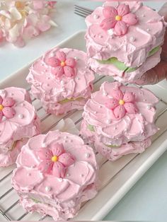 pink frosted cupcakes on a cooling rack with flowers in the middle and one being held by someone's hand