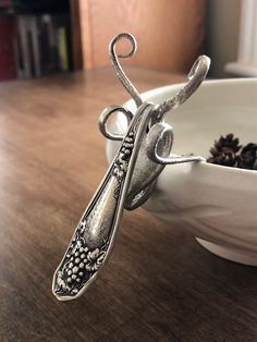 a silver spoon sitting on top of a wooden table next to a bowl filled with pine cones