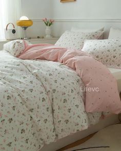 a bed with pink and white comforters in a room next to a lamp on a table