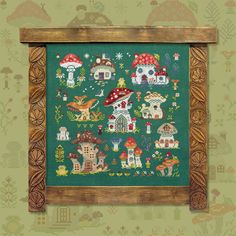 a cross - stitch pattern with houses and mushrooms on green fabric in a wooden frame