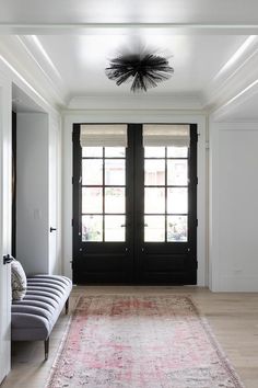 a large rug in the middle of a room with two black doors and a bench