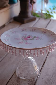 a glass cake plate with pink flowers and tassels on the edge sitting on a wooden table