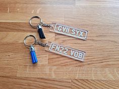 two metal keychains with blue tassels are on a wooden surface,