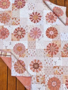 a pink and white quilt with flowers on it sitting on top of a wooden floor