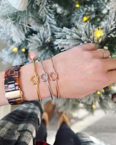 a woman's arm with three bracelets on it and a christmas tree in the background