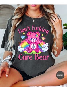 Indulge in rebellious comfort with our "I Don't Care Bear Vibes" T-shirt! This whimsical tee features a cheeky care bear boldly expressing your carefree attitude with a pair of unmistakable middle fingers and a vibrant rainbow backdrop. Crafted from soft, breathable fabric, this shirt guarantees both style and comfort. Embrace the carefree spirit and make a statement with this playful addition to your wardrobe. It's not just a shirt; it's an expression of your "don't give a care" attitude! *Unisex Sizing* Trendy Crew Neck T-shirt With Bear Print, Cute Bear Print Crew Neck T-shirt, Trendy Short Sleeve T-shirt With Bear Print, Graphic Tee With Bear Print For Streetwear, Casual Bear Print T-shirt For Streetwear, Black Casual T-shirt With Bear Print, Rainbow Backdrop, Middle Fingers, Rainbow Tee