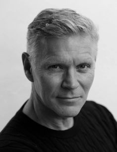 a black and white photo of a man with blonde hair looking at the camera while wearing a sweater