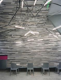 chairs are lined up in front of a wall with lines on it and lights hanging from the ceiling