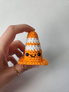 a hand holding a small orange and white crocheted hat with eyes on it