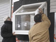 two men working on a window in front of a house