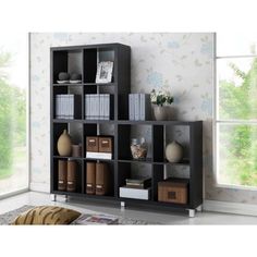 a bookshelf filled with lots of books in front of a window next to a vase