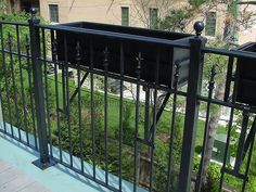 an iron fence on the side of a building next to a green lawn and trees