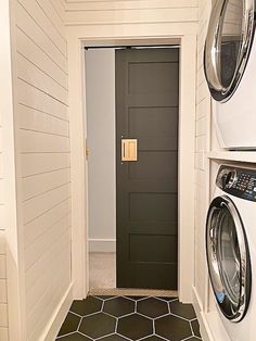 a washer and dryer in a room with white walls, black door and tile floor