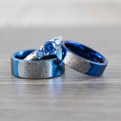 two wedding rings with blue and white designs on them sitting on a wooden table next to each other