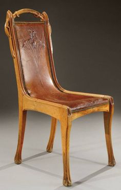 an antique wooden chair with brown leather upholstered back and arm rests against a gray background