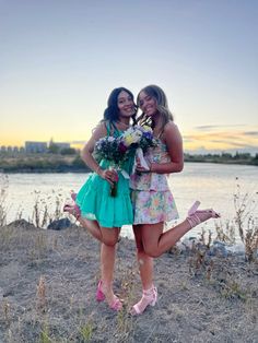 two young women standing next to each other on a beach near the water at sunset