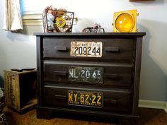 a wooden dresser with two license plates on it's drawers in a room next to a window