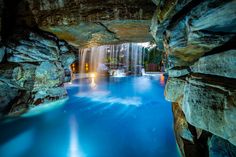 a pool in the middle of some rocks with water coming from it and lights on