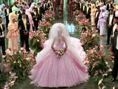 a woman in a pink wedding dress surrounded by other people and flowered archways